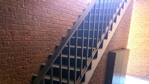 A staircase with metal railings and a carpeted floor, leading to a room with a brick wall. - Holbrook Town Centre Motor Inn (Holbrook)