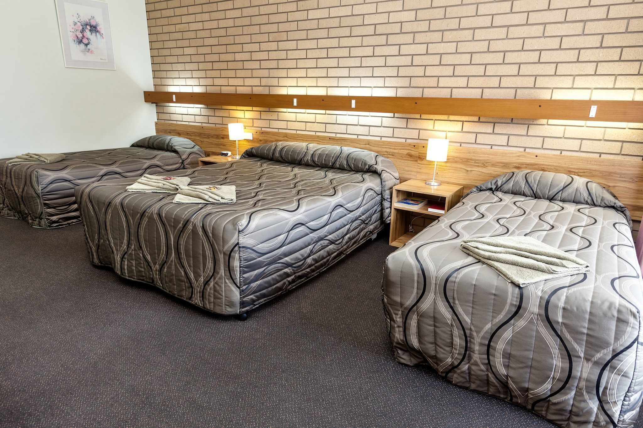 A hotel room with three beds, each with a unique patterned bedspread.