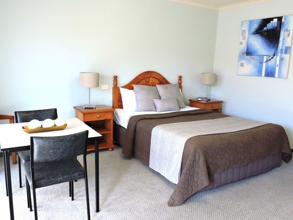 A bedroom with a bed, two bedside tables, a desk, and a chair.