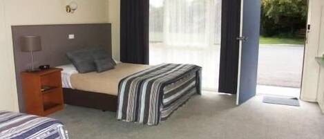 A hotel room with a bed, a nightstand, a lamp, and a view of the outside.