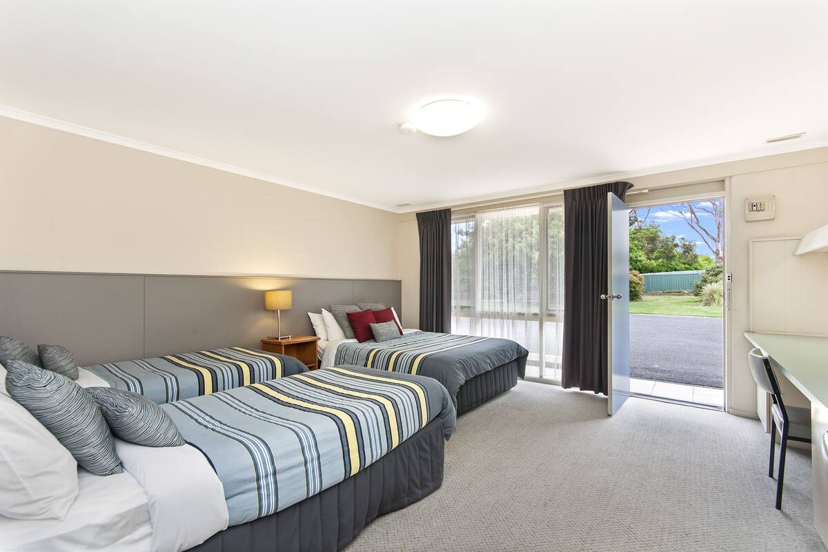 A hotel room with two beds, a desk, and a view of the outdoors.
