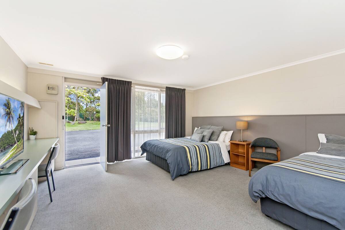 A hotel room with two beds, a desk, a TV, and a sliding glass door to the outside.