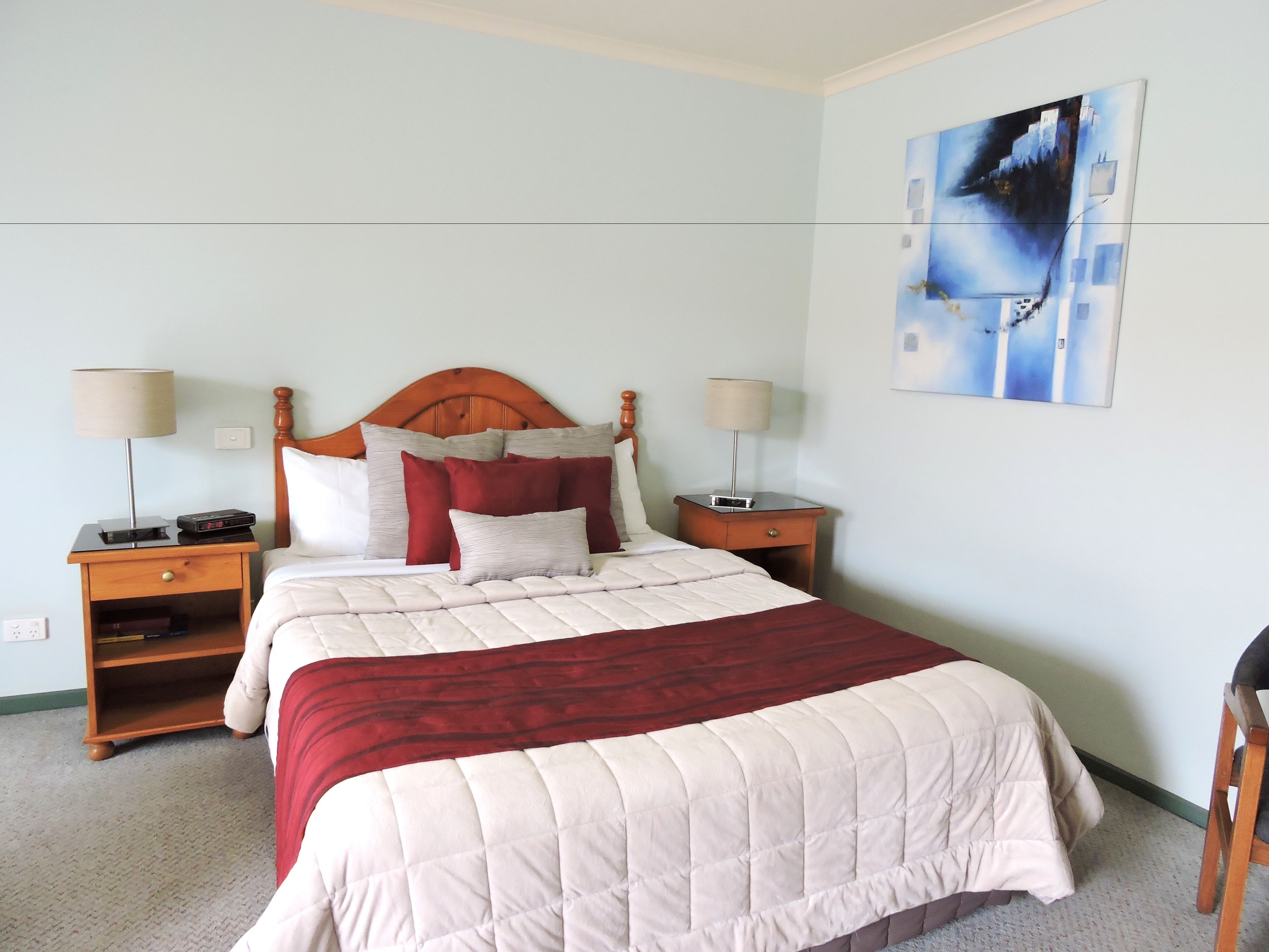 Une chambre à coucher avec une tête de lit en bois, un grand lit avec de nombreux oreillers, deux tables de chevet avec des lampes et un tableau au mur.