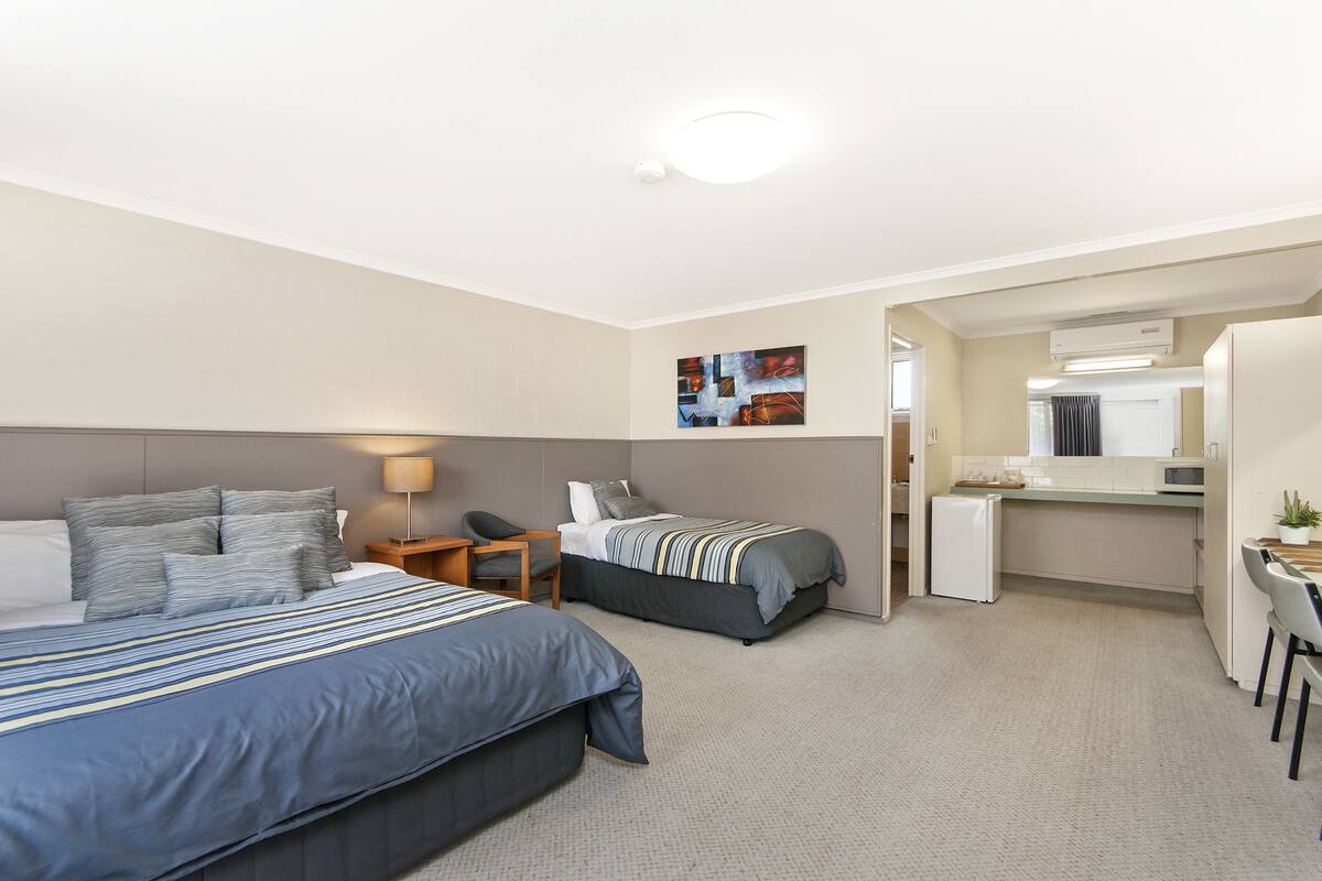A hotel room with two beds, a desk, a refrigerator, and a kitchenette.