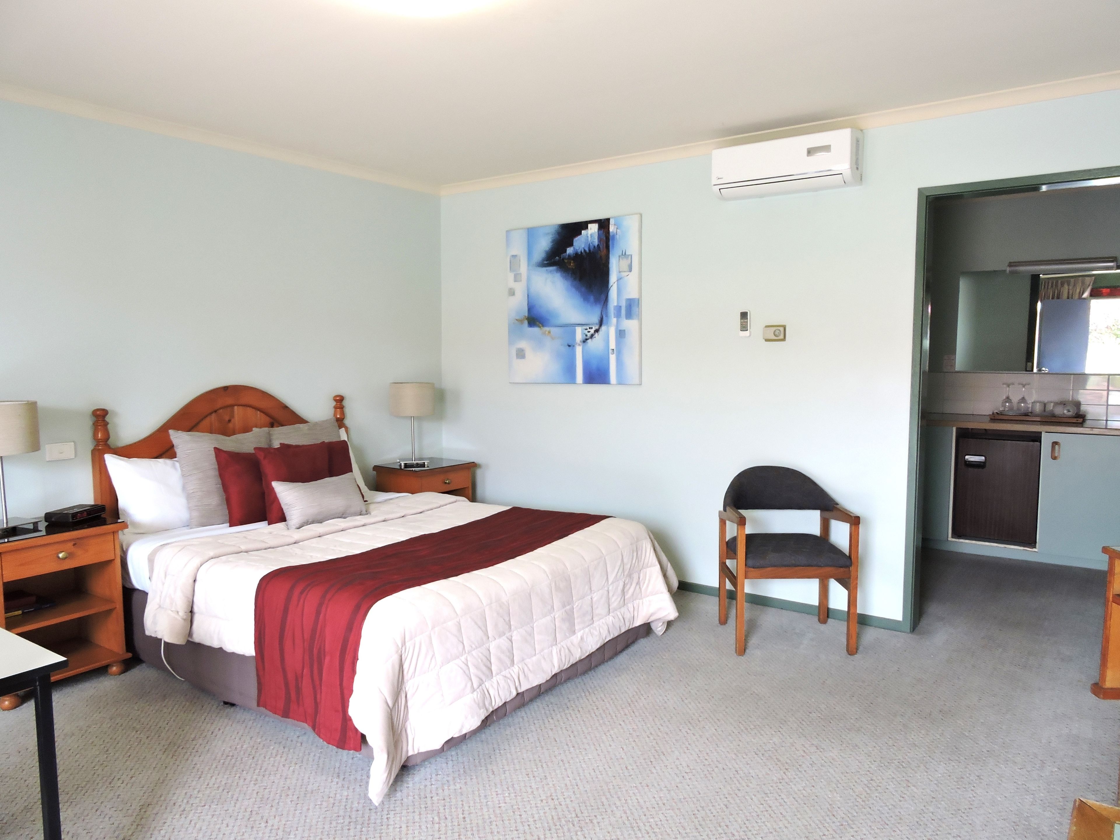 A hotel room with a bed, bedside tables, a chair, a desk, and a kitchenette.