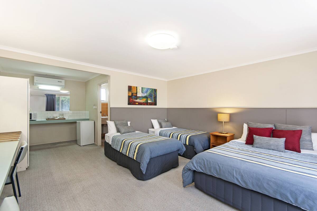 A hotel room with two beds, a desk, a small kitchenette, and a bathroom.