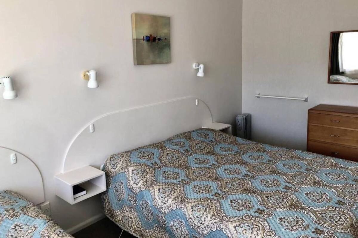Een slaapkamer met een bed, nachtkastjes, een kaptafel, een wandlamp en een schilderij.