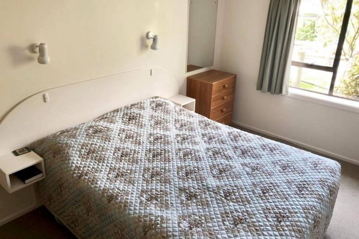 Een slaapkamer met een bed, een dressoir, een spiegel en een raam met gordijnen.