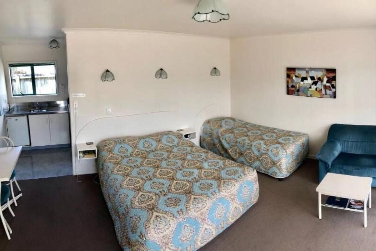 Een kleine kamer met twee bedden, een tafeltje, een bank en een kitchenette.