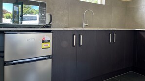 Eine moderne Küche mit integriertem Mikrowellenherd, einem Edelstahl-Kühlschrank, einer Spüle mit modernem Wasserhahn und dunklen Holzschränken.