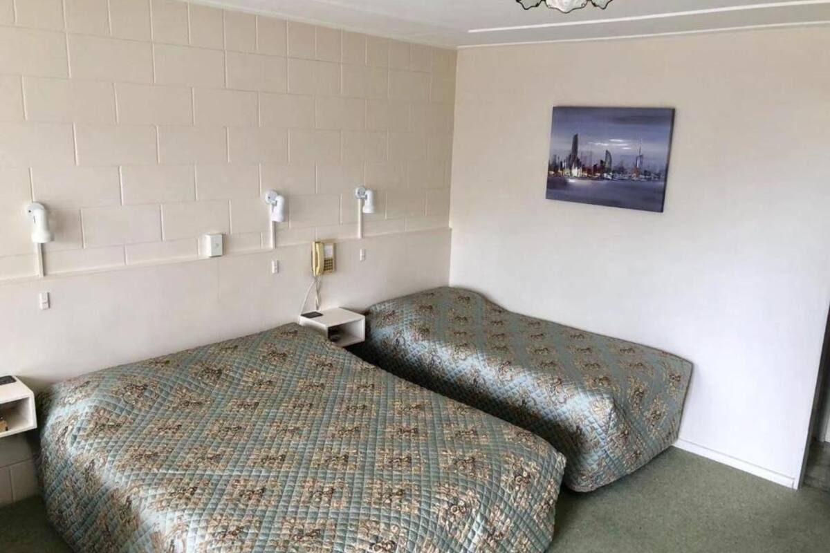 Een kamer met twee bedden, een stadsgezichtschilderij aan de muur en een hoofdbord met een bakstenen patroon.