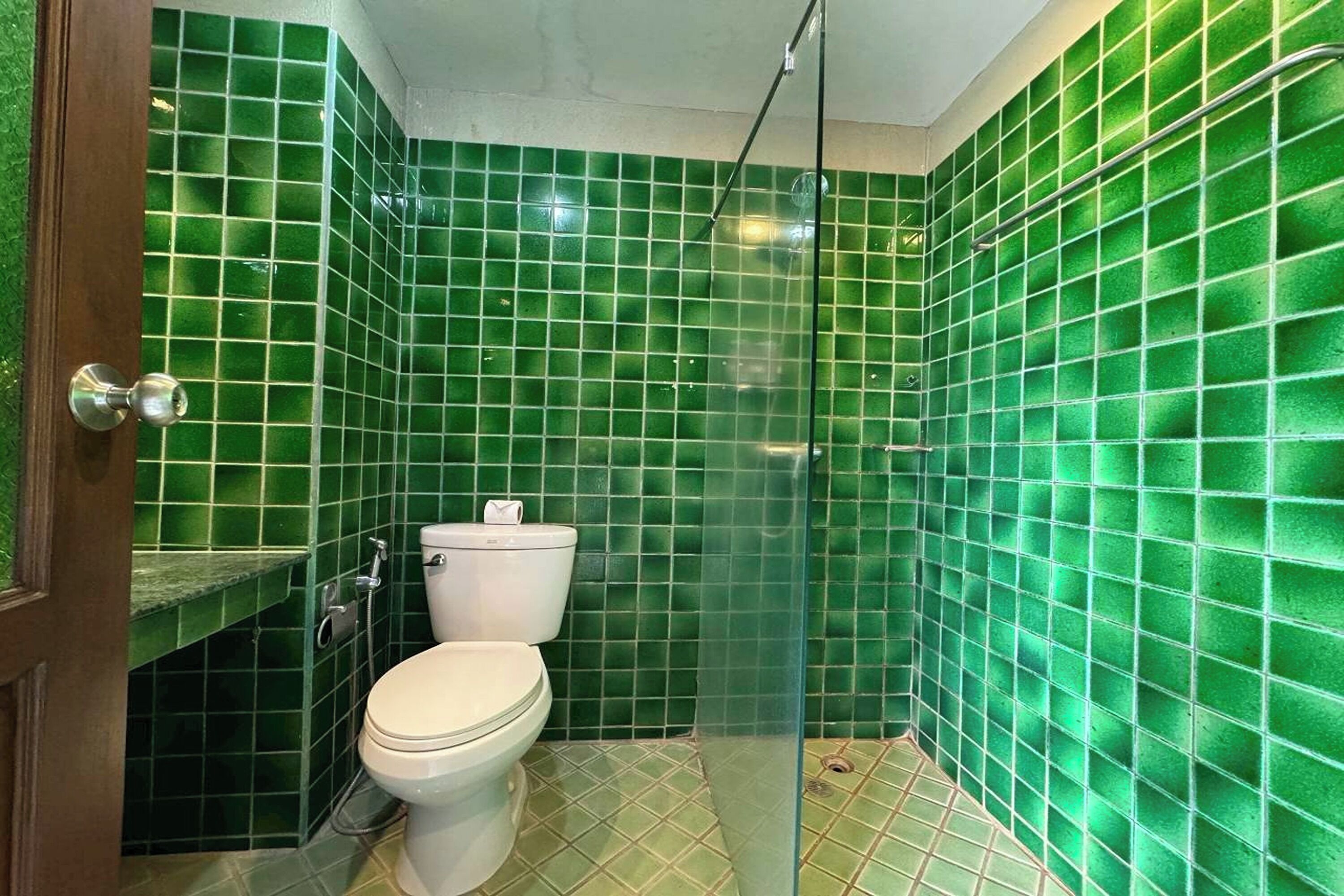 A bathroom with green tiled walls, a white toilet, and a glass shower enclosure.
