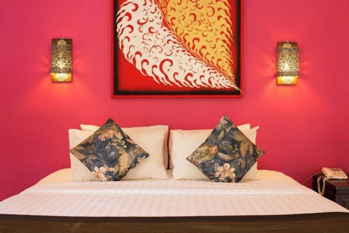 A bed with floral pillows, a red wall, and two wall-mounted light fixtures.