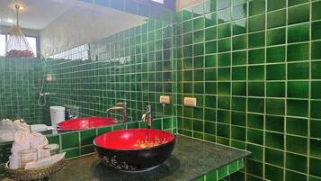 Un baño con paredes cubiertas de azulejos verdes, dos lavabos, un espejo y una lámpara colgante.
