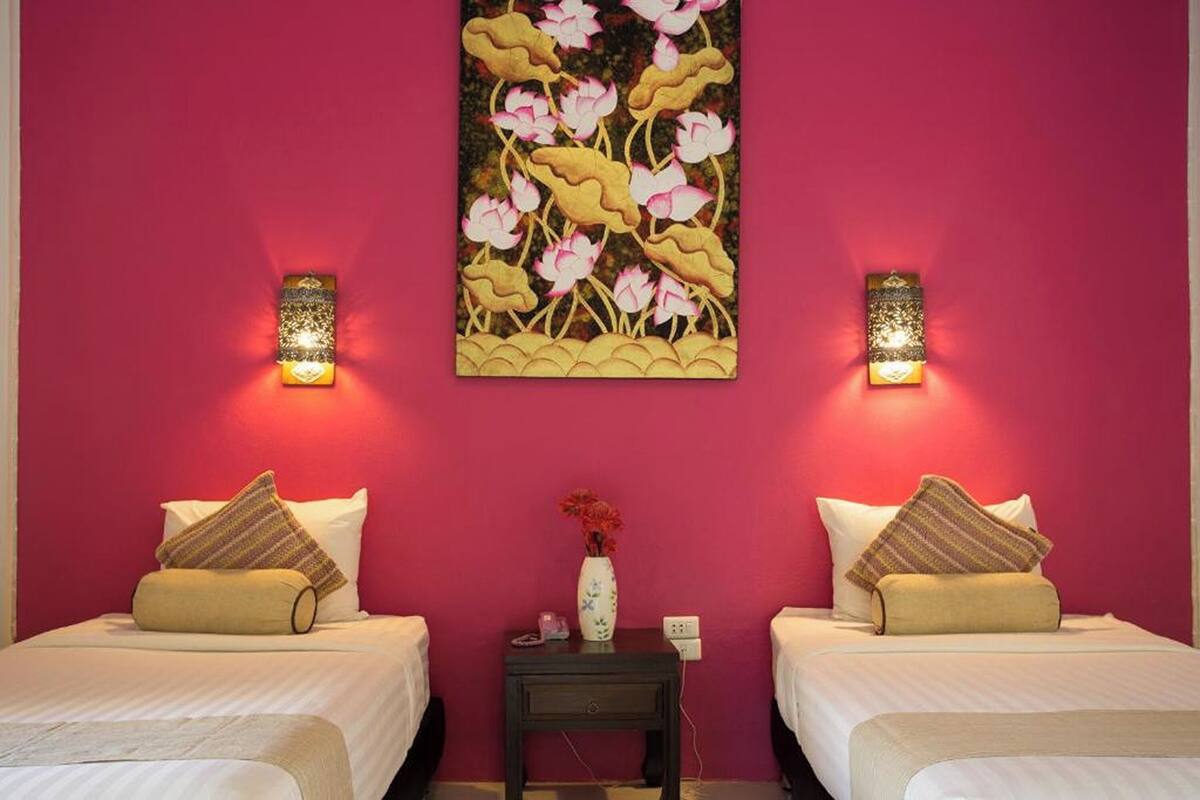 A room with two beds, a nightstand with a vase, and wall-mounted lights.