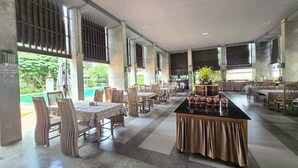 A spacious dining area with multiple tables and chairs, large windows, and a central island with decorative items. - Poonyamantra Resort Chiang Rai (Mae Sai)