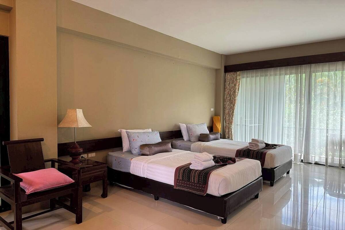 A hotel room with two beds, a chair, a nightstand, and a lamp.