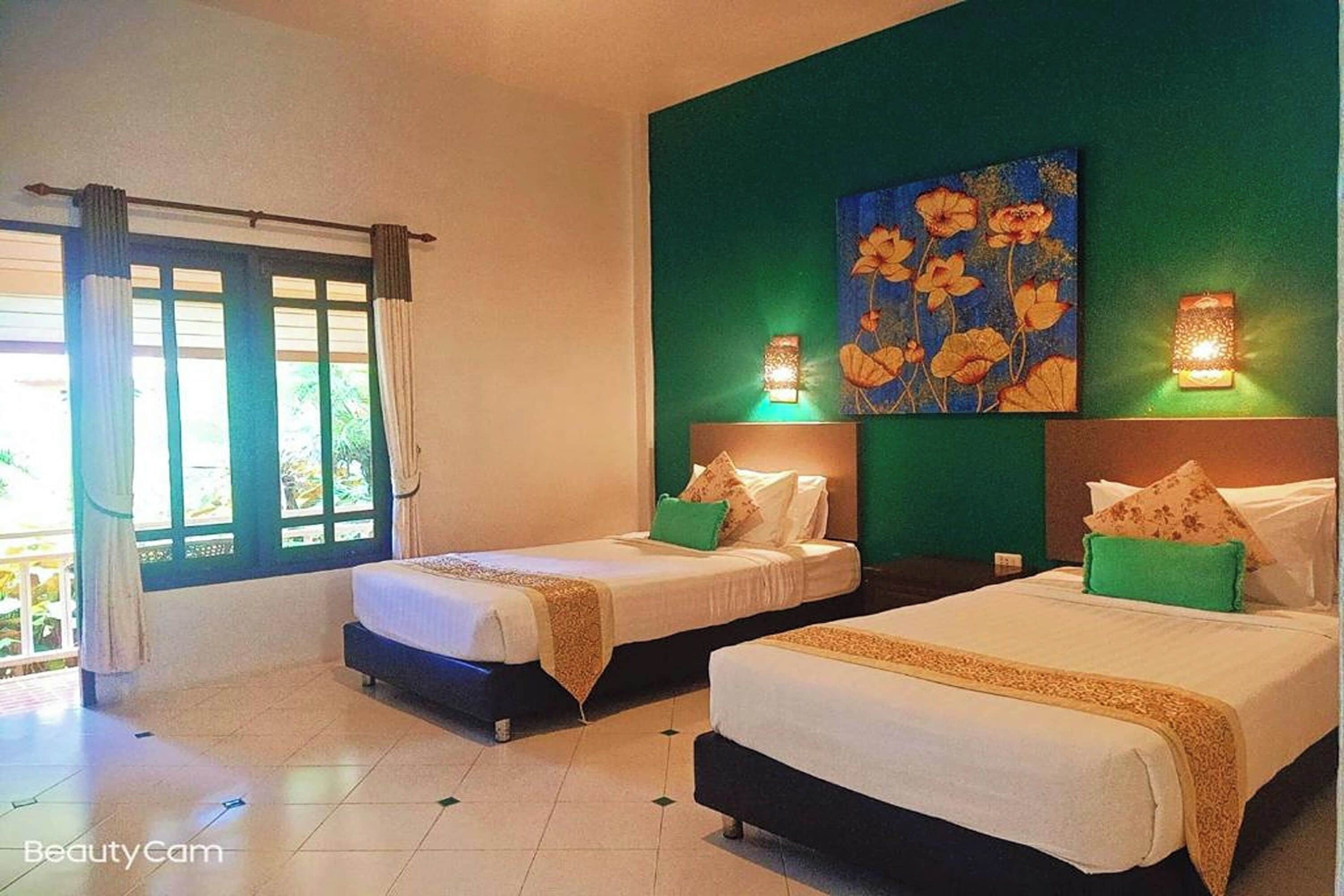 Habitación de hotel con dos camas, una pared verde decorativa y un cuadro sobre las camas.