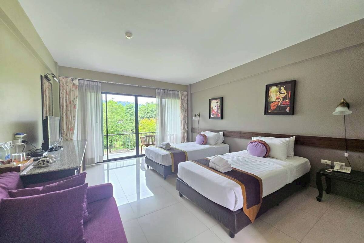 A hotel room with two beds, a desk, a chair, a balcony with curtains, and a painting on the wall.