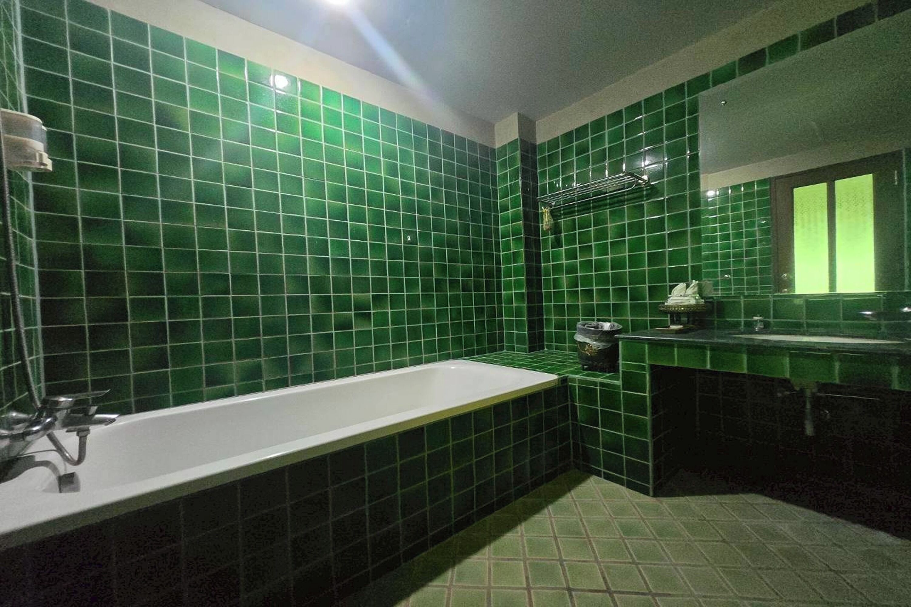 Une salle de bain avec des carreaux verts, une baignoire blanche, un lavabo et un miroir.