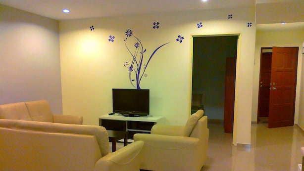 Una sala de estar con un conjunto de sofá, un televisor sobre un mueble bajo y una puerta que da a otra habitación.