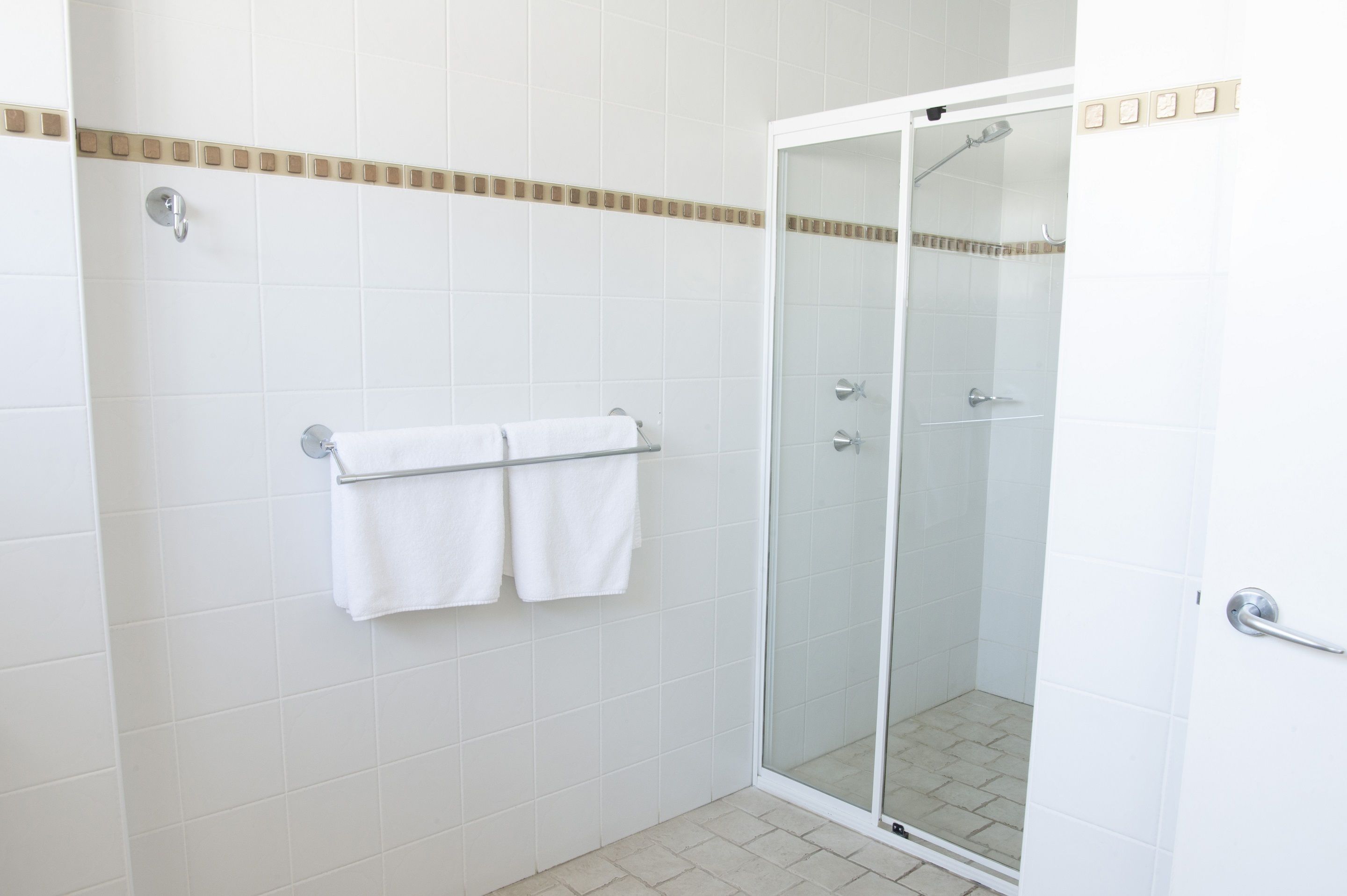 A modern bathroom with white tiles, a glass shower enclosure, and a towel rack with two white towels.