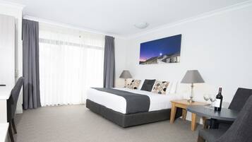 A hotel room with a bed, two bedside tables, a chair, a desk, and a painting on the wall.