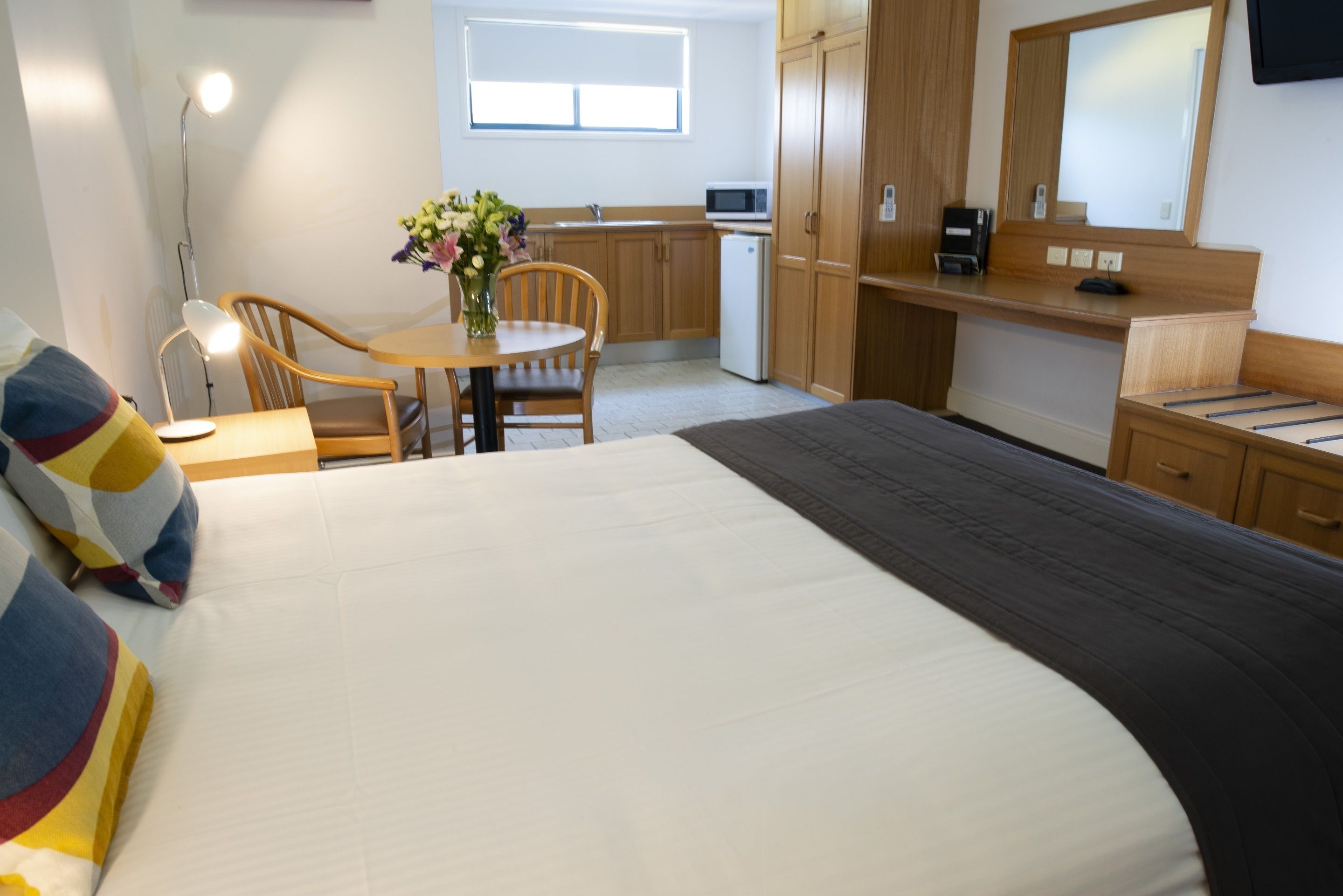 A hotel room with a bed, a desk, a chair, a small kitchen area, and a bathroom.