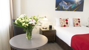 Une chambre d’hôtel avec un lit, une table de chevet avec une lampe, un vase de fleurs et un tableau au mur.