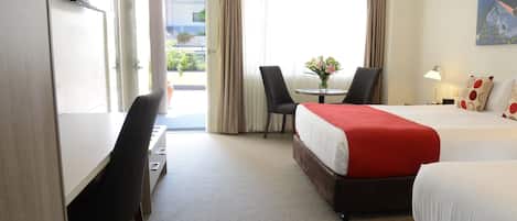 Una habitación de hotel con dos camas, un escritorio, una silla, un televisor y un ventanal con cortinas.