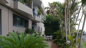 Un bâtiment moderne doté de balcons, d’un patio aménagé avec du mobilier d’extérieur et de diverses plantes tropicales.