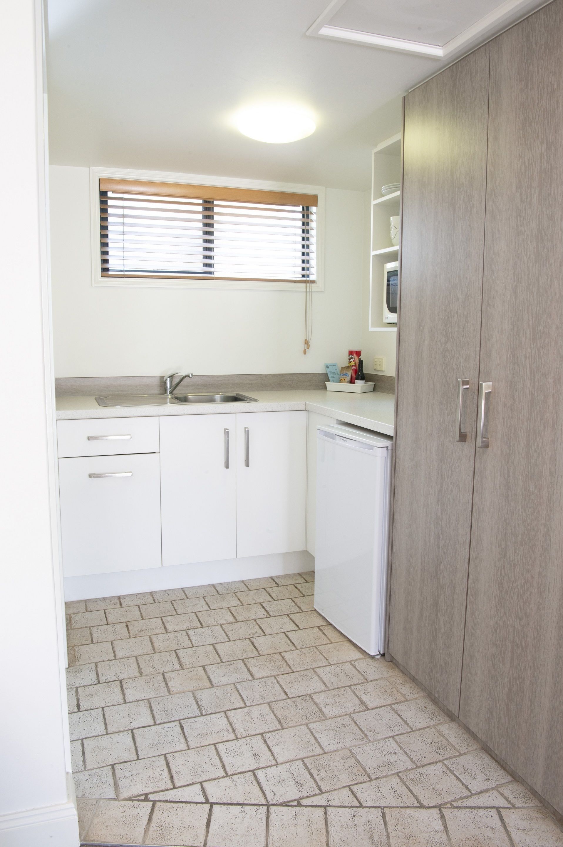 A compact kitchen with white cabinets, a built-in dishwasher, and a window with blinds.