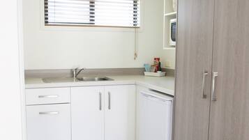 A compact kitchen with white cabinets, a built-in dishwasher, and a window with blinds.