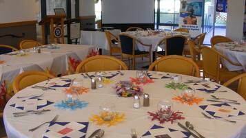 Un salón de conferencias con mesas redondas preparadas para una reunión, equipado con tarjetas de identificación, vasos de agua y cubiertos.