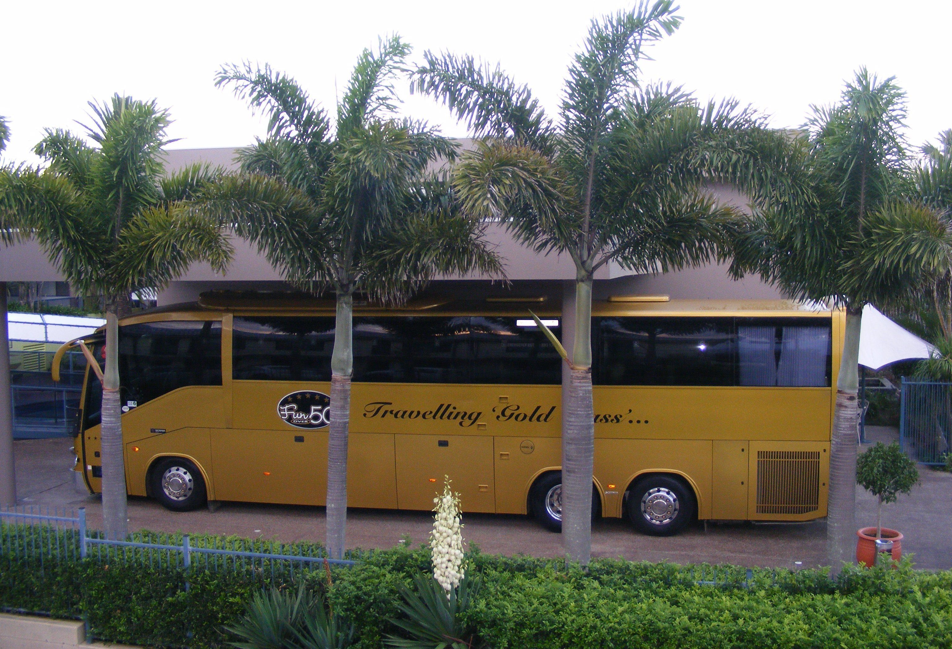 Een gele bus met 'Travelling Gold' erop geparkeerd voor een gebouw.
