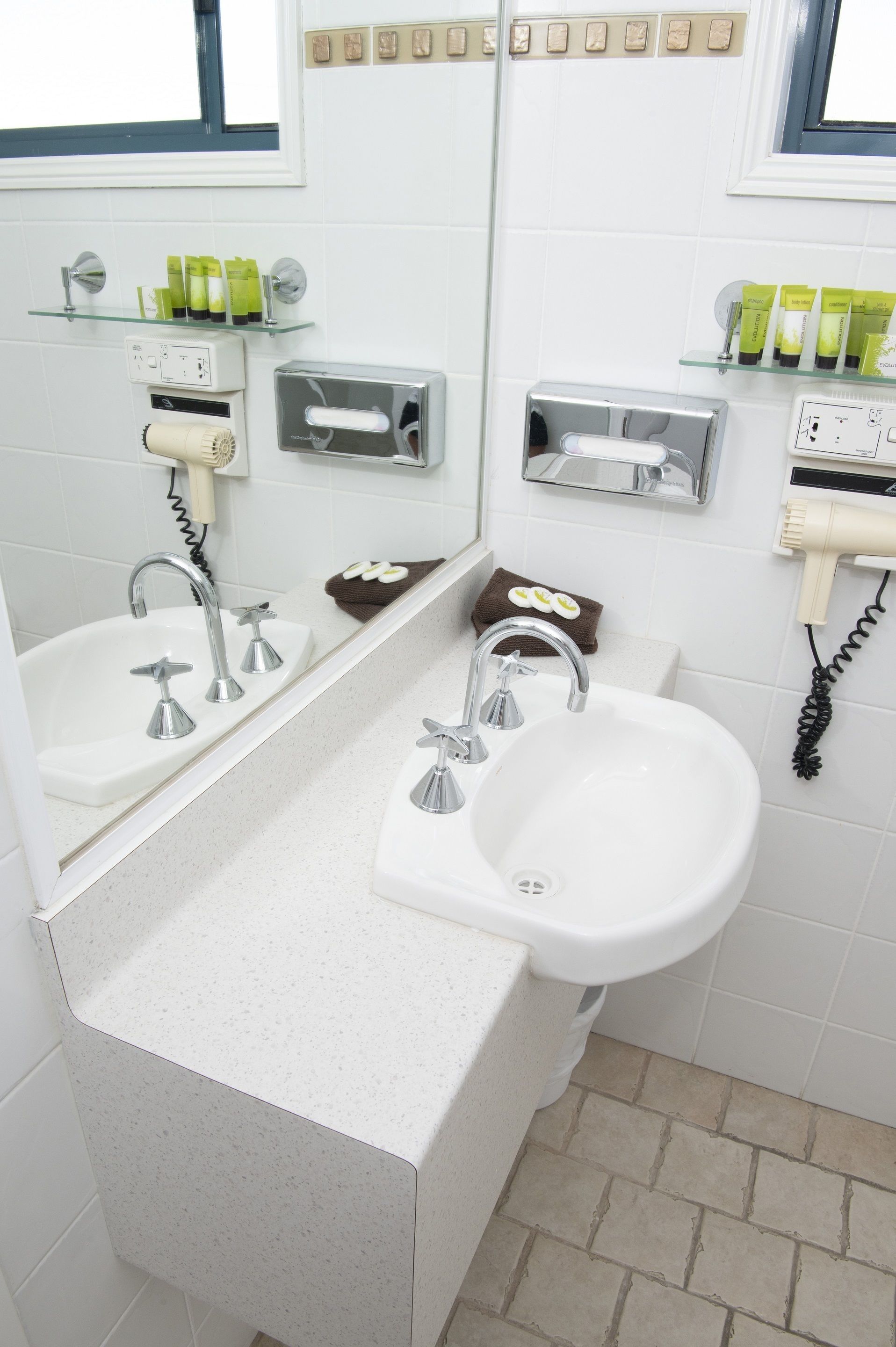 A modern bathroom with two sinks, a hairdryer, and toiletries on shelves.