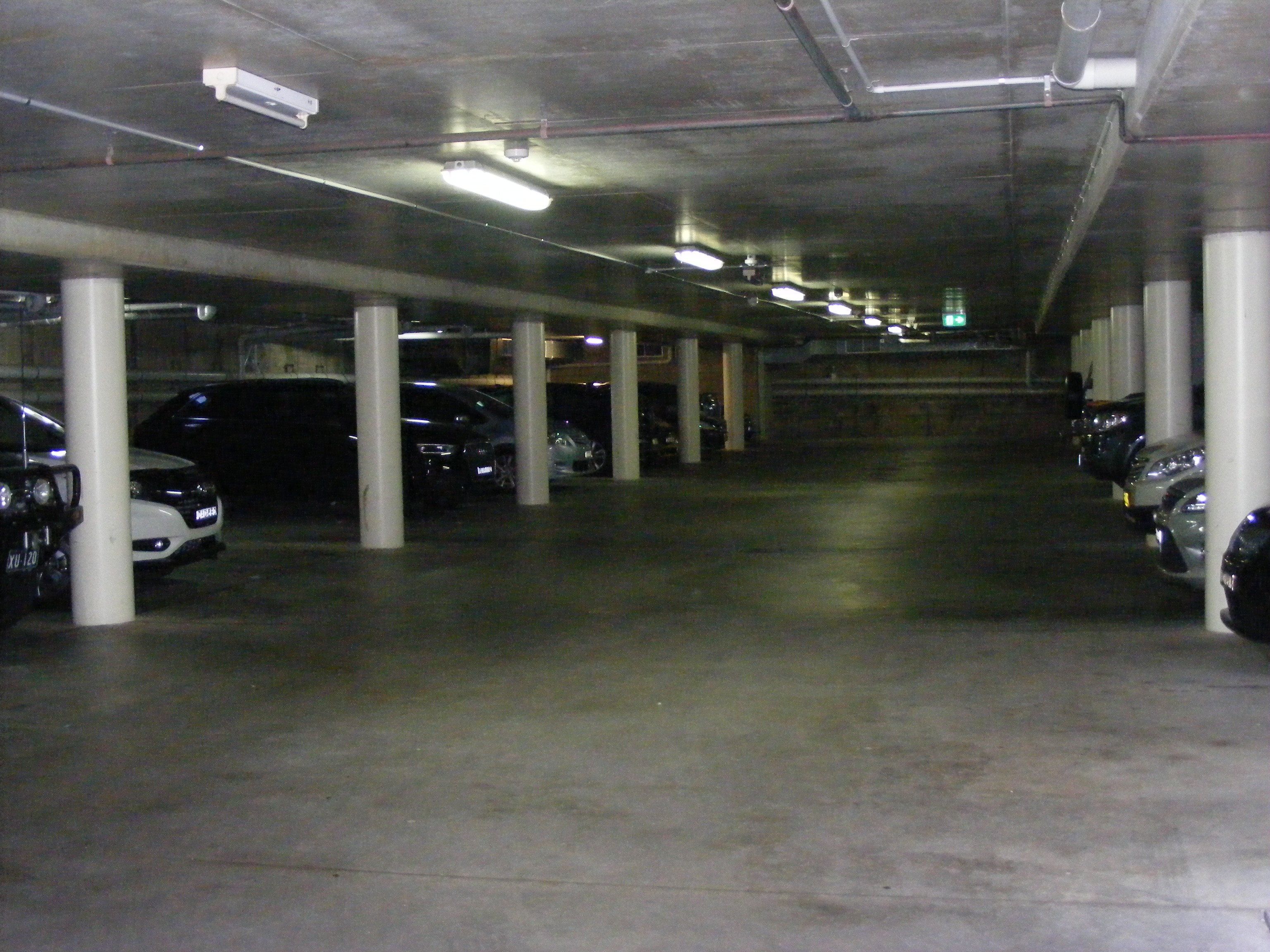 A multi-level parking garage with concrete pillars and fluorescent lighting.
