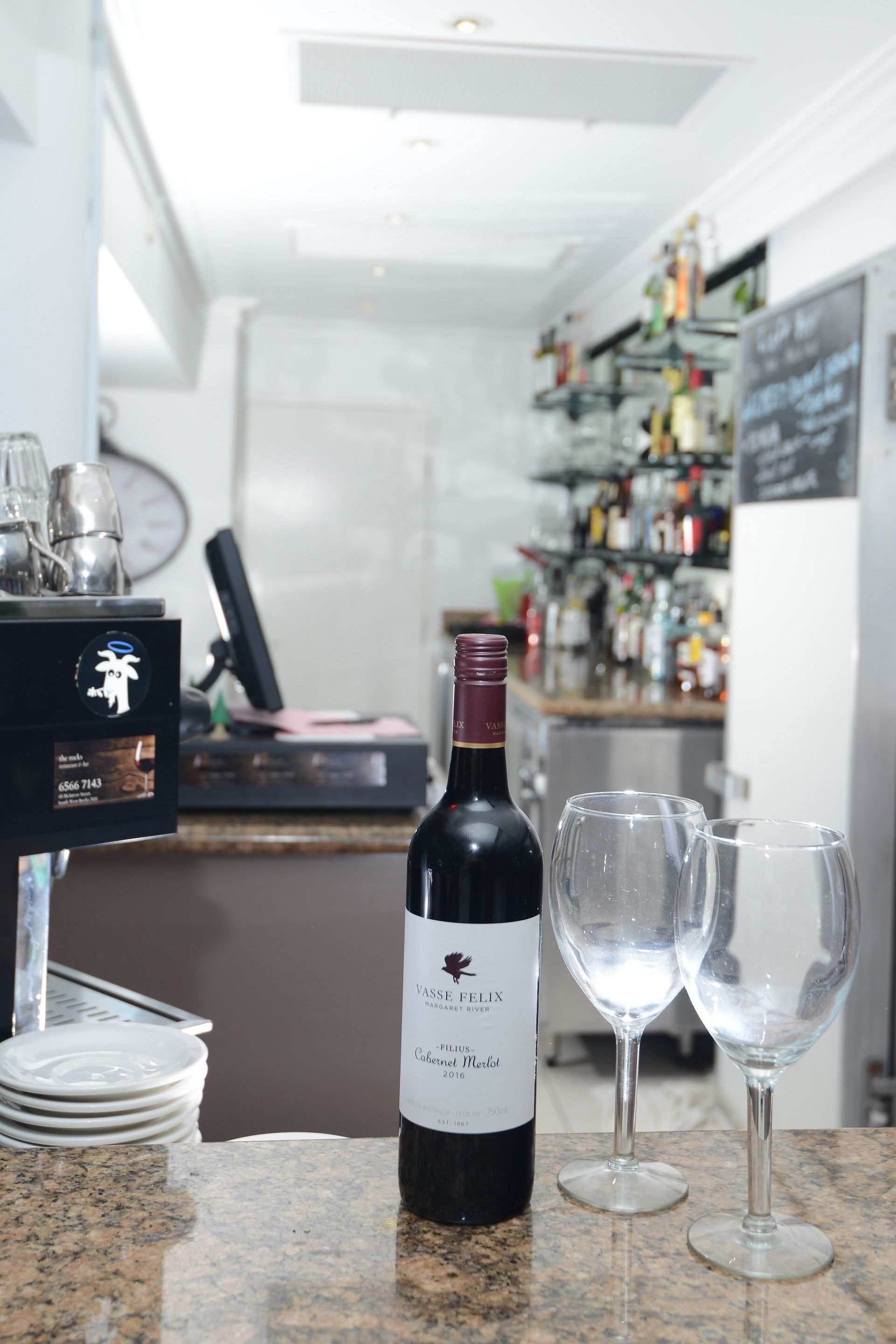 A wine bottle and two glasses on a counter with a bar in the background.