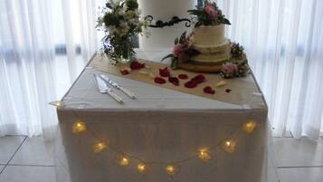 A wedding cake on a table with a white tablecloth, surrounded by flowers and rose petals.