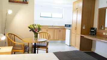 Una cocina compacta con armarios de madera, una mesa de comedor con sillas, un jarrón de flores y un microondas.