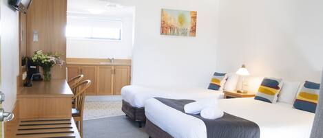 A hotel room with two beds, a desk, and a chair. There is a painting on the wall and a window providing natural light.