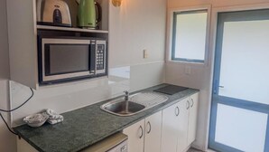 A kitchen with a microwave, kettle, and sink. - Avana Suites (Lower Hutt)