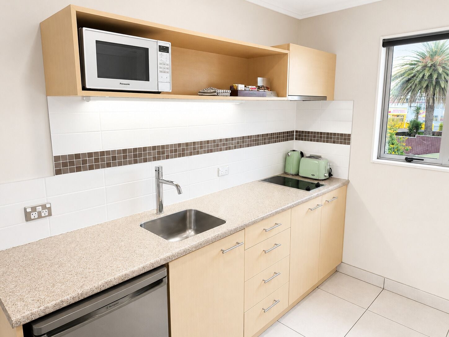 A kitchen with a built-in microwave, a sink, and a window with a view of palm trees.