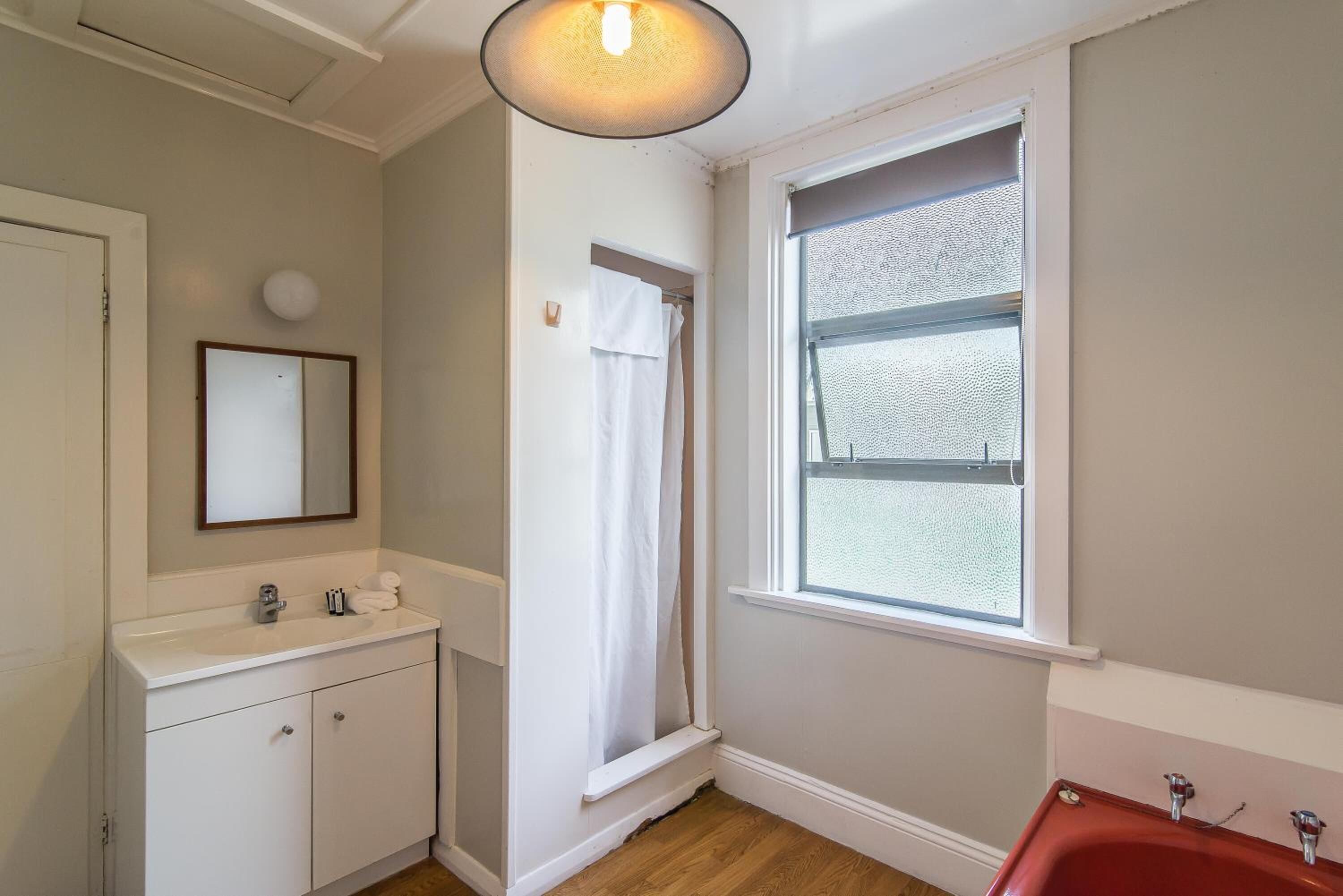 A bathroom with a white sink, a mirror, a window with a view, and a red bathtub.