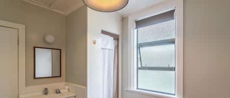 A bathroom with a white sink, a mirror, a window with a view, and a red bathtub.
