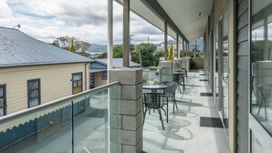 A covered outdoor area with a glass railing, stone pillars, and tables with chairs. - Avana Suites (Lower Hutt)