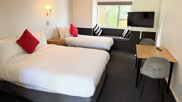 A hotel room with two beds, a TV, a desk, and a window. - Avana Suites (Lower Hutt)