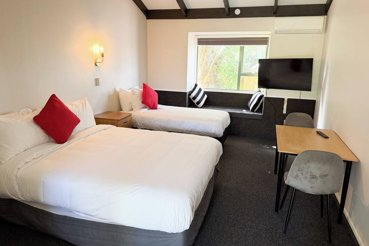 A hotel room with two beds, a TV, a desk, and a window.