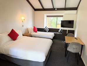 A hotel room with two beds, a TV, a desk, and a window. - Avana Suites (Lower Hutt)