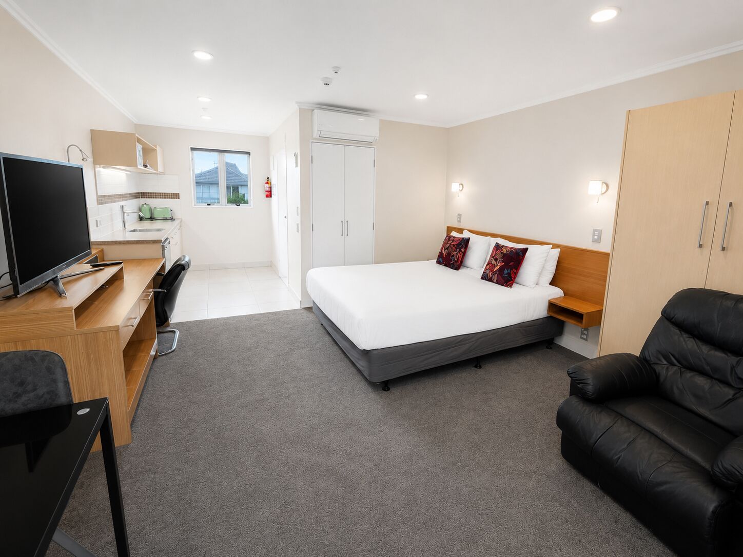 Een hotelkamer met een bed, een bureau met televisie, een stoel, een kledingkast en een kleine kitchenette.